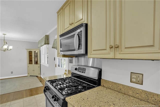 kitchen with a chandelier, light stone countertops, stainless steel appliances, cream cabinetry, and ornamental molding