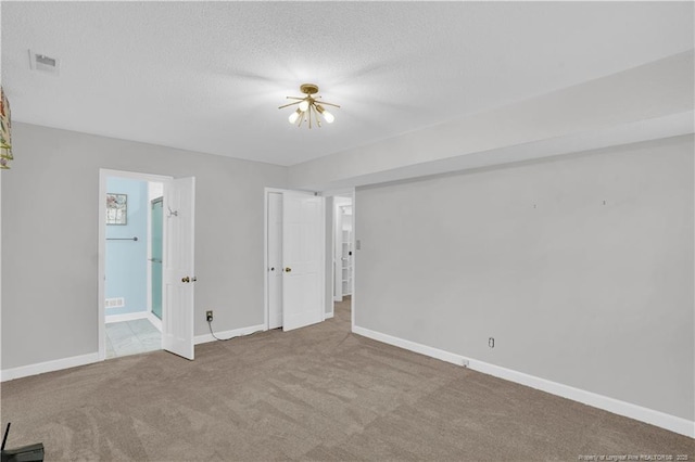 spare room featuring baseboards, carpet floors, a textured ceiling, and visible vents