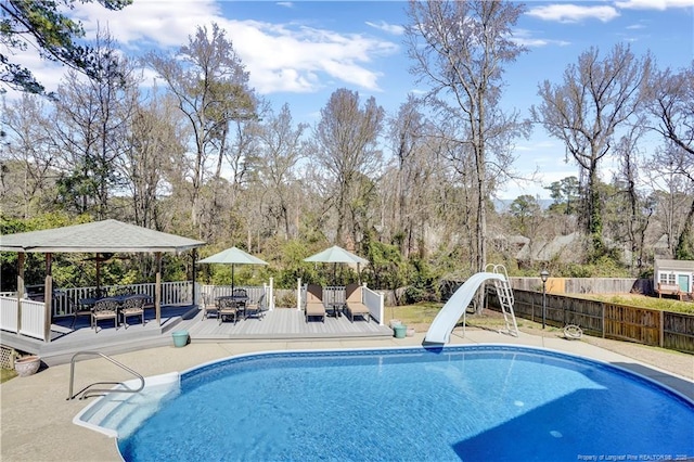view of pool with fence, a water slide, a fenced in pool, outdoor dining space, and a deck