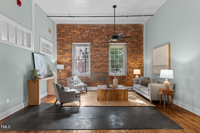 living area with track lighting, baseboards, hardwood / wood-style floors, and brick wall