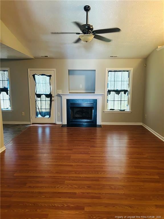 unfurnished living room featuring ceiling fan, a healthy amount of sunlight, wood finished floors, and baseboards