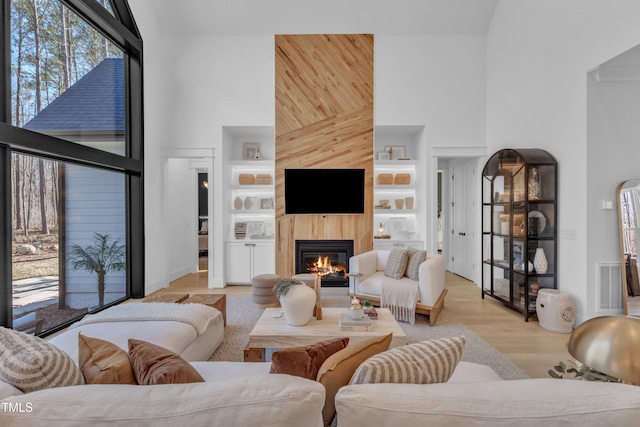 living room featuring visible vents, a glass covered fireplace, built in features, light wood-style floors, and a high ceiling