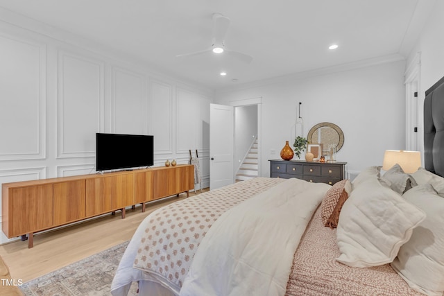 bedroom featuring a ceiling fan, a decorative wall, ornamental molding, and light wood finished floors