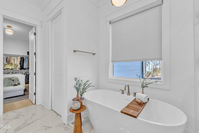 bathroom with marble finish floor and a freestanding tub
