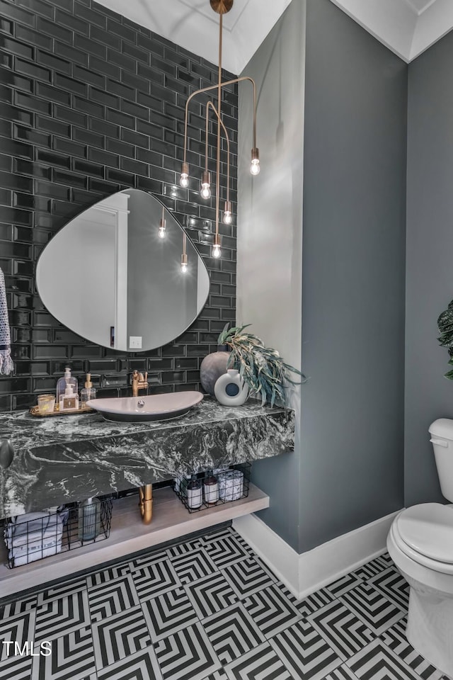 half bathroom with tile patterned flooring, toilet, baseboards, decorative backsplash, and a sink