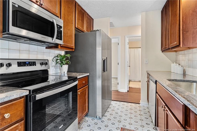 6611 Brannan Way, Fayetteville, NC 28314 - kitchen featuring stainless steel appliances, light flooring, brown cabinets, backsplash, and a textured ceiling