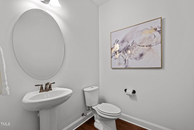 bathroom featuring baseboards, wood finished floors, toilet, and a sink
