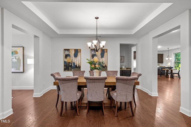 dining space featuring a chandelier, a tray ceiling, and dark wood finished floors
