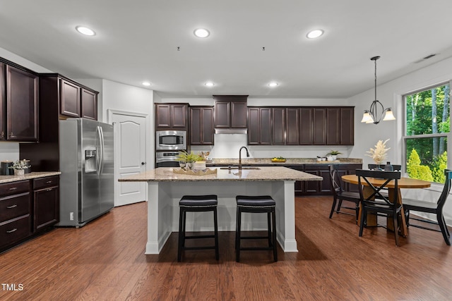 kitchen featuring appliances with stainless steel finishes, dark brown cabinets, light stone counters, dark wood finished floors, and a breakfast bar