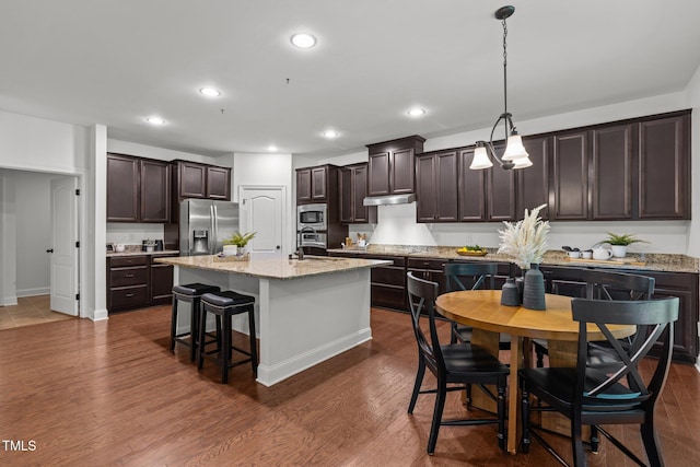 kitchen with stainless steel appliances, dark brown cabinetry, dark wood finished floors, a breakfast bar, and under cabinet range hood