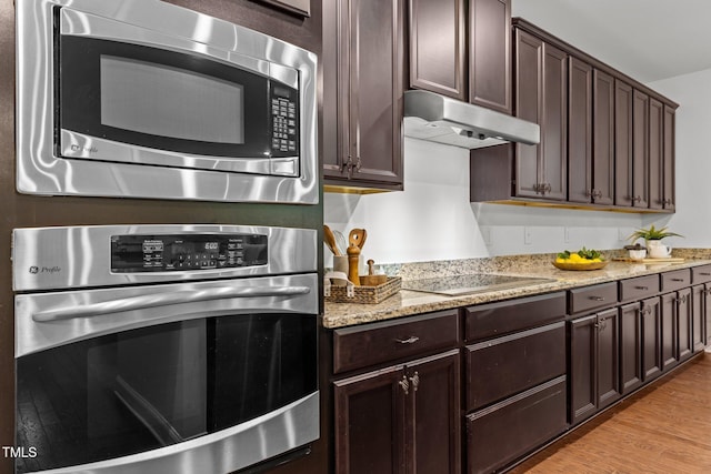 kitchen featuring appliances with stainless steel finishes, under cabinet range hood, dark brown cabinets, light wood-style floors, and light stone counters