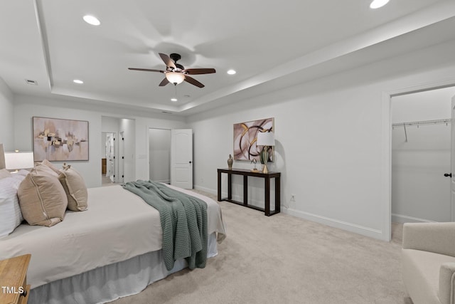 bedroom with recessed lighting, a raised ceiling, light colored carpet, baseboards, and a walk in closet