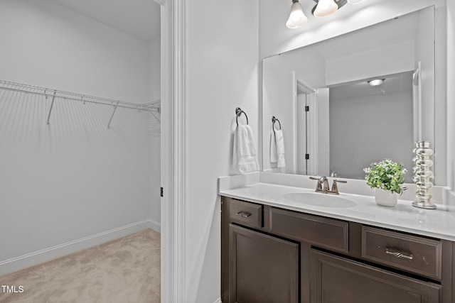 bathroom with a spacious closet, vanity, and baseboards