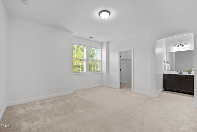 unfurnished bedroom with light carpet, a sink, a spacious closet, and baseboards