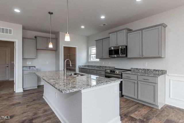 kitchen featuring appliances with stainless steel finishes, a sink, gray cabinets, a center island with sink, and dark wood finished floors