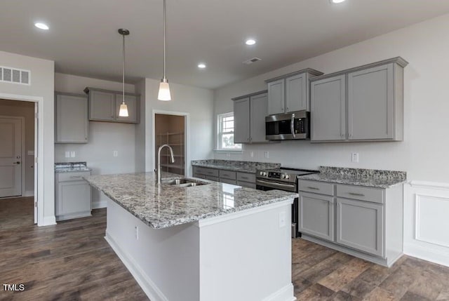 kitchen with appliances with stainless steel finishes, a sink, gray cabinets, an island with sink, and dark wood-type flooring