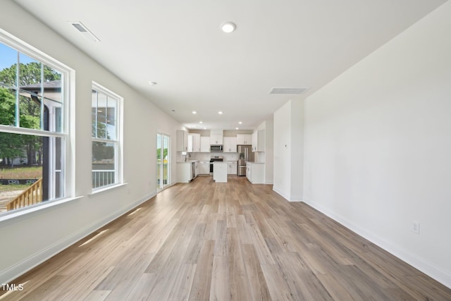 unfurnished living room featuring light wood-type flooring, healthy amount of natural light, baseboards, and recessed lighting