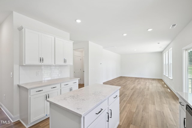 kitchen featuring light wood-style floors, decorative backsplash, white cabinetry, light stone countertops, and a kitchen island