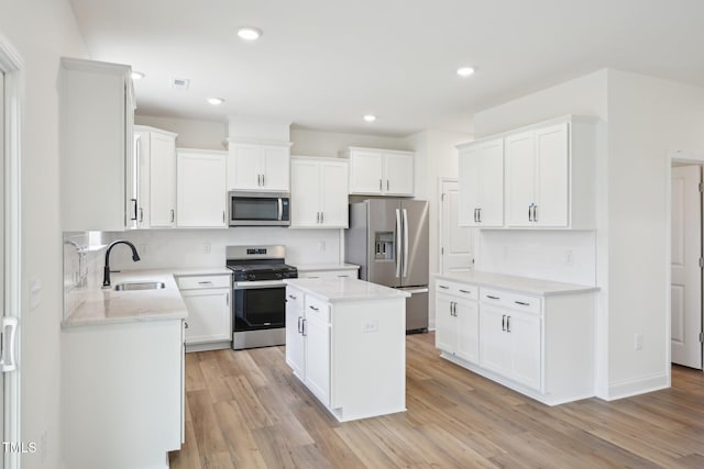 kitchen with stainless steel appliances, a sink, decorative backsplash, light wood finished floors, and white cabinets