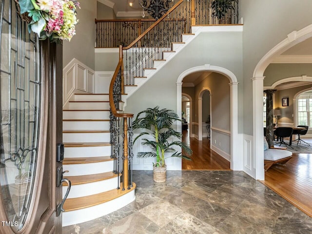 foyer featuring arched walkways, a high ceiling, crown molding, and stairs