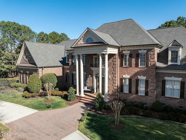 greek revival house with roof with shingles, a front yard, and brick siding