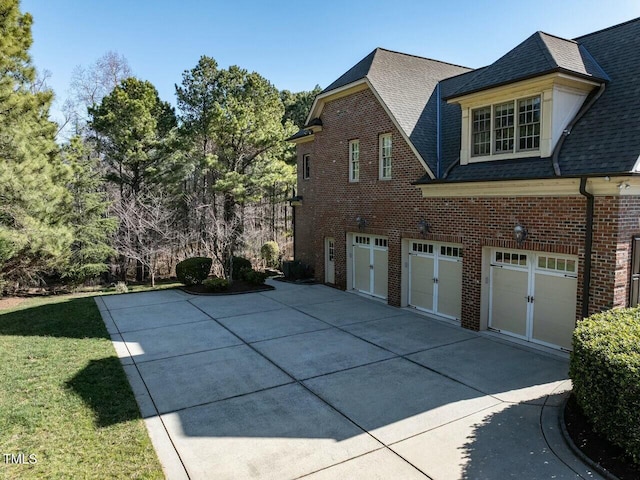 view of side of home featuring a garage, brick siding, a shingled roof, and a lawn