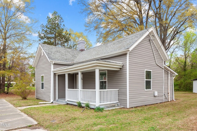 view of side of home with roof with shingles, a chimney, a lawn, and covered porch