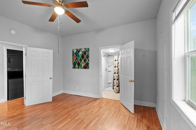 unfurnished room with light wood finished floors, stacked washer / drying machine, baseboards, and ceiling fan