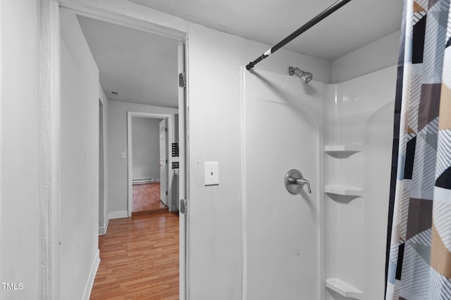 bathroom with a shower, baseboard heating, baseboards, and wood finished floors
