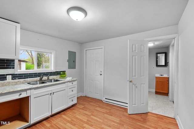 kitchen with light wood-type flooring, electric panel, a sink, a baseboard radiator, and decorative backsplash