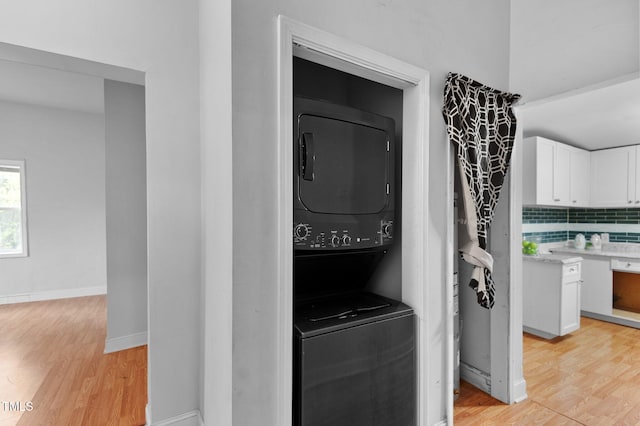 washroom featuring baseboards, light wood-type flooring, stacked washing maching and dryer, and laundry area