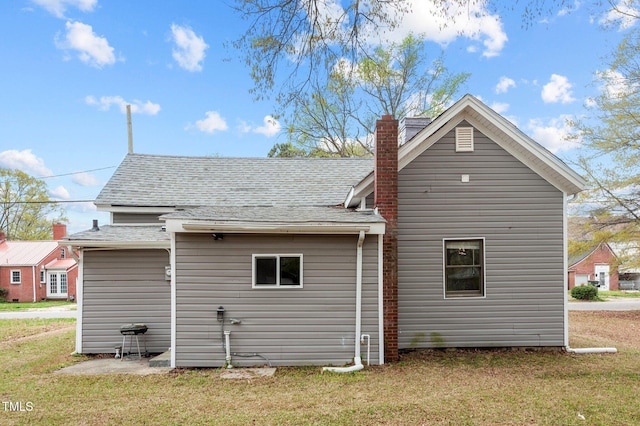 back of house with roof with shingles, a lawn, and a chimney