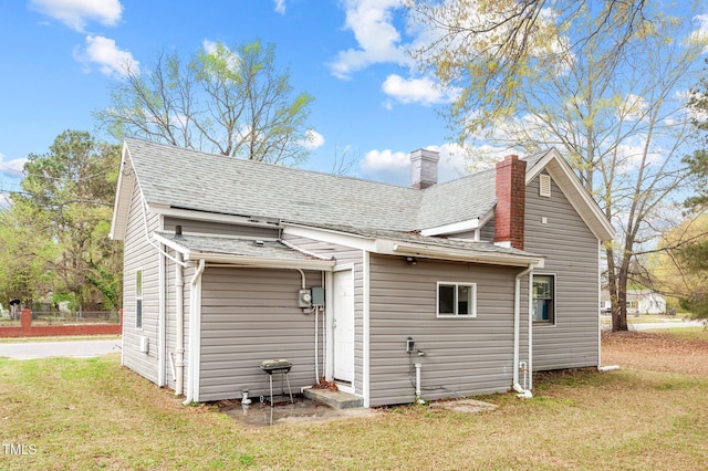 back of house with a yard, a shingled roof, and a chimney