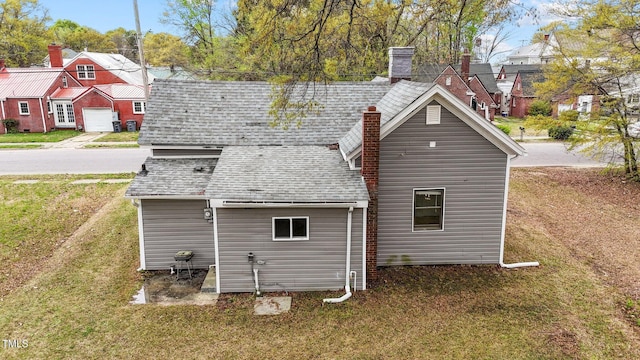 rear view of property with a chimney, a shingled roof, a residential view, and a lawn