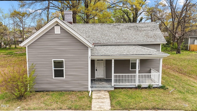 view of front facade featuring a front yard, a porch, a shingled roof, and a chimney