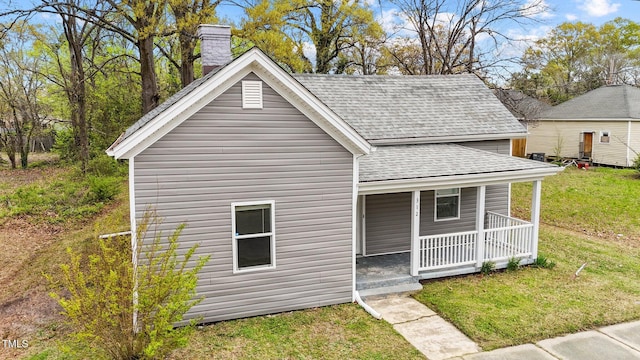 view of front of home featuring a shingled roof, covered porch, a front lawn, and a chimney
