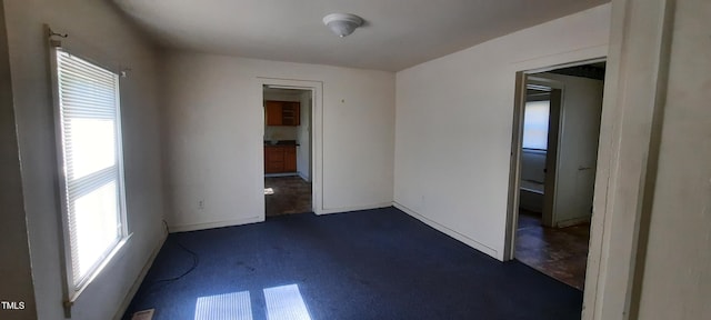 unfurnished room with dark carpet, a wealth of natural light, and baseboards