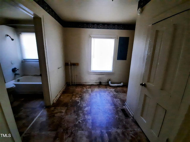 interior space with electric panel, shower / washtub combination, toilet, and a healthy amount of sunlight