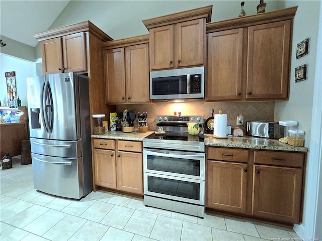 921 Satinwood Ct, Fayetteville, NC 28312 - kitchen featuring appliances with stainless steel finishes, decorative backsplash, vaulted ceiling, light stone countertops, and light tile patterned floors