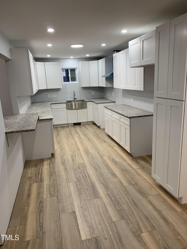 kitchen featuring recessed lighting, light stone counters, a sink, and light wood-type flooring