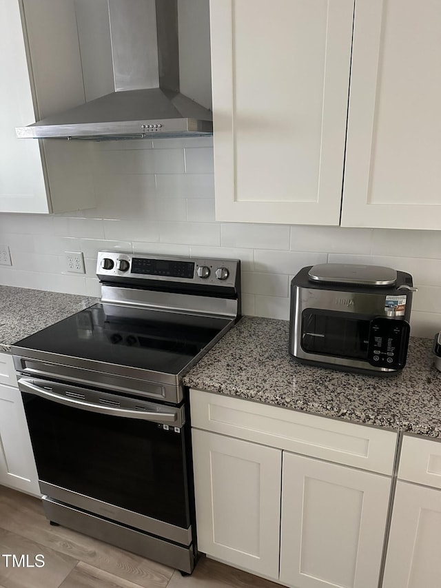 kitchen featuring wall chimney range hood, stainless steel range with electric cooktop, white cabinetry, and tasteful backsplash