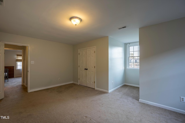 carpeted spare room featuring baseboards, visible vents, and plenty of natural light