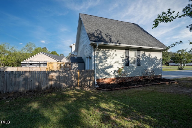 view of side of property with a lawn, fence, and roof with shingles