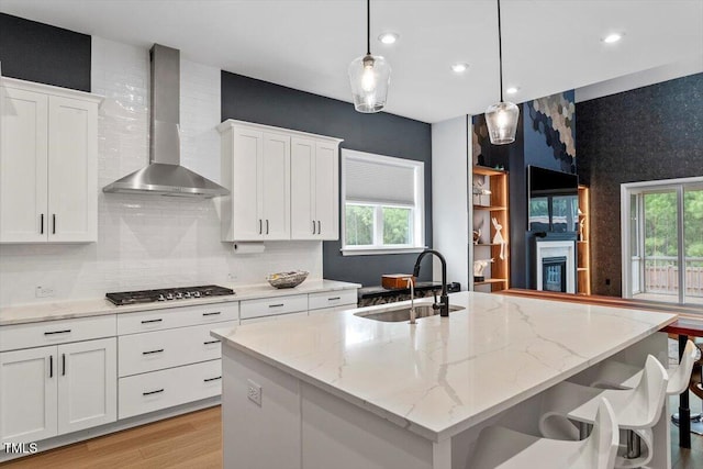 956 The Parks Dr, Pittsboro, NC 27312 - kitchen featuring an island with sink, white cabinetry, wall chimney exhaust hood, stainless steel gas stovetop, and a sink