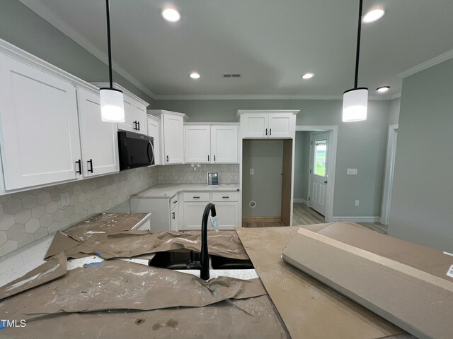 502 S Vance St, Fremont, NC 27830 - kitchen featuring black microwave, crown molding, backsplash, white cabinetry, and light stone counters