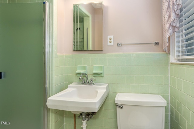 bathroom with a sink, tile walls, toilet, and wainscoting