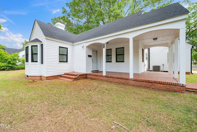 view of front of home with central air condition unit, a shingled roof, a chimney, and a front lawn