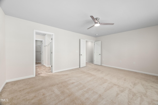 unfurnished bedroom with baseboards, a walk in closet, light carpet, and a ceiling fan