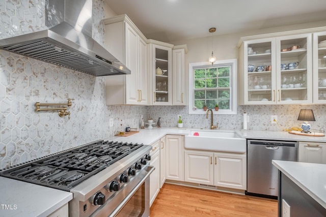 kitchen featuring wall chimney exhaust hood, a sink, light countertops, light wood-type flooring, and stainless steel appliances