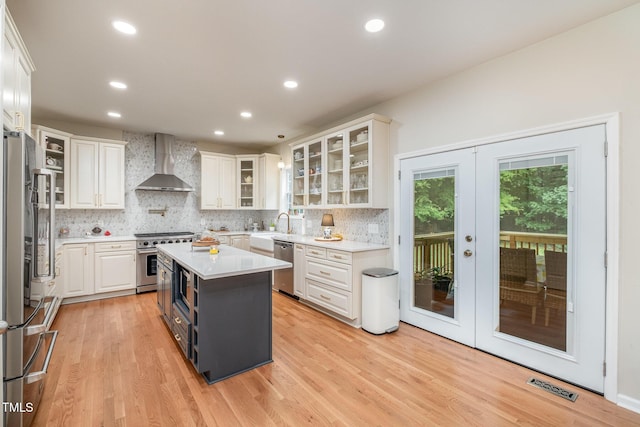 kitchen featuring wall chimney range hood, white cabinets, visible vents, appliances with stainless steel finishes, and french doors